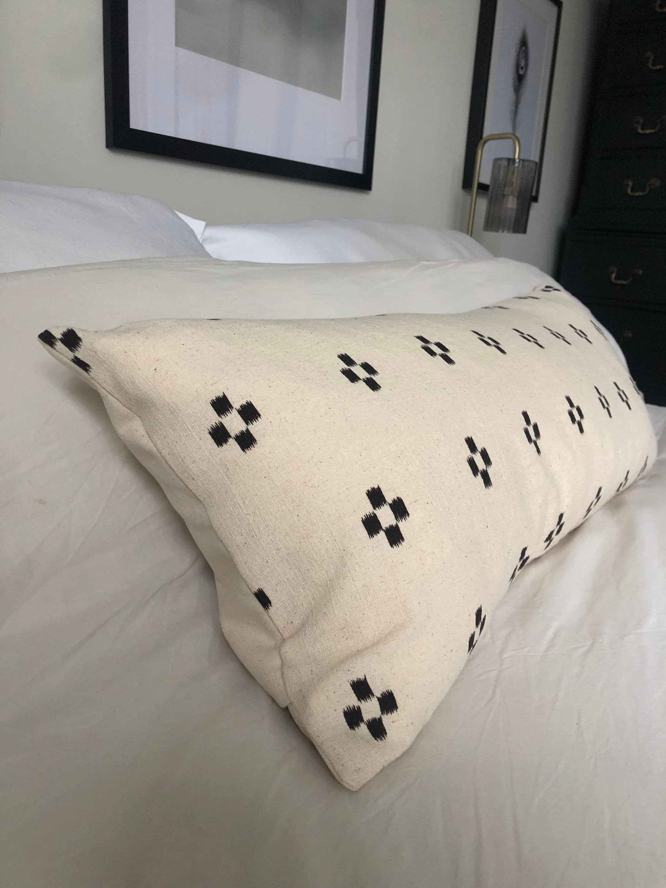 Beige patterned ikat pillow with black patterns on a bed in a bedroom setting