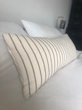Striped neutral and black pillow on a bed with a neutral background