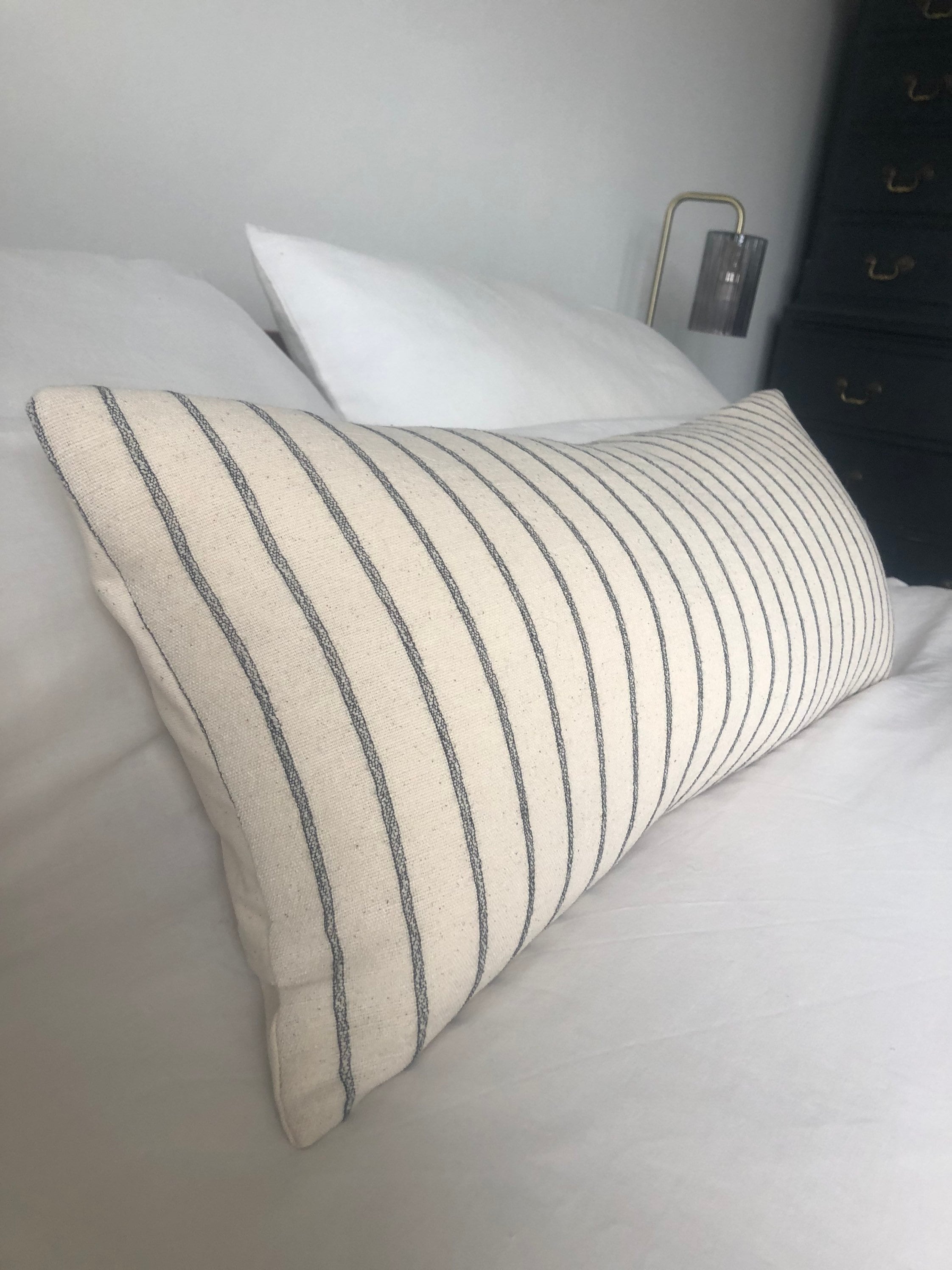 Striped neutral and black pillow on a bed with a neutral background