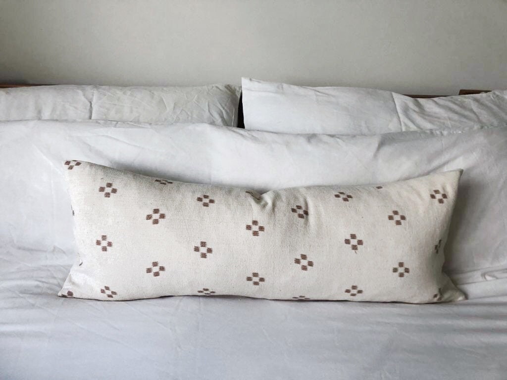 Decorative pillow with warm brown geometric pattern on a bed with white bedding.
