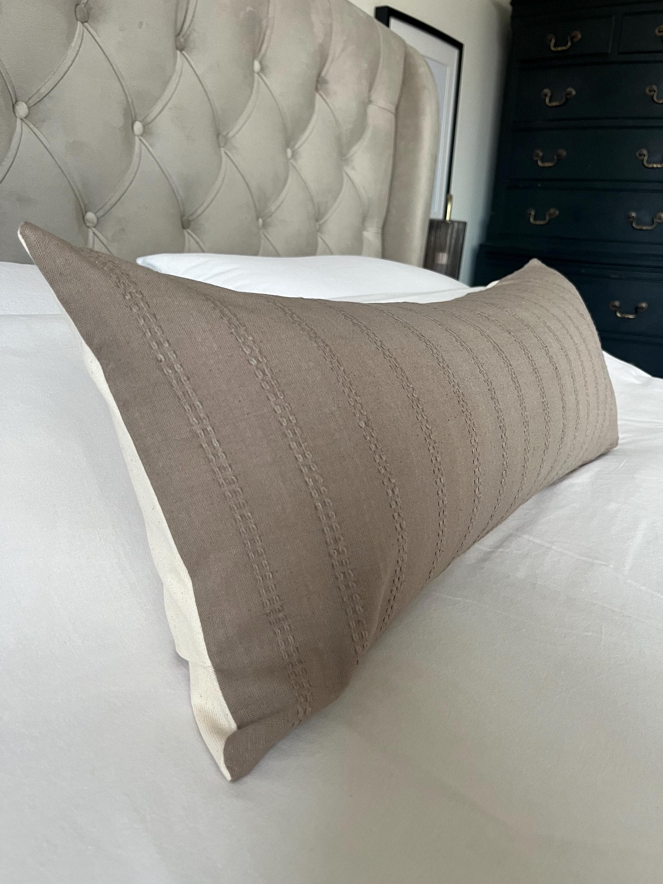 Beige pillow on a bed with a tufted headboard and dresser in the background