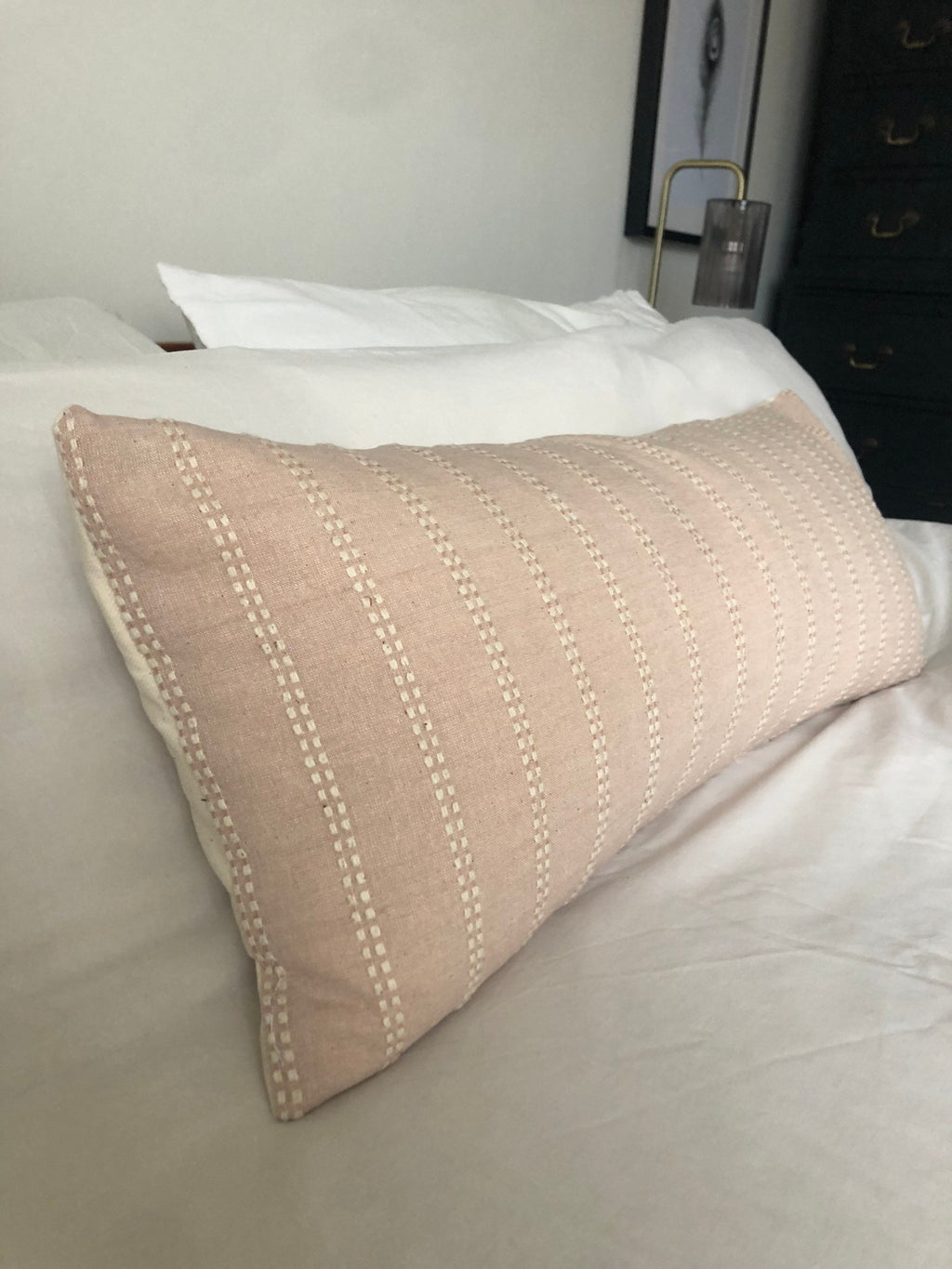 pink pillow with white stitching on a bed in a bedroom setting.
