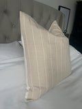 Beige striped pillow on a bed with a tufted headboard