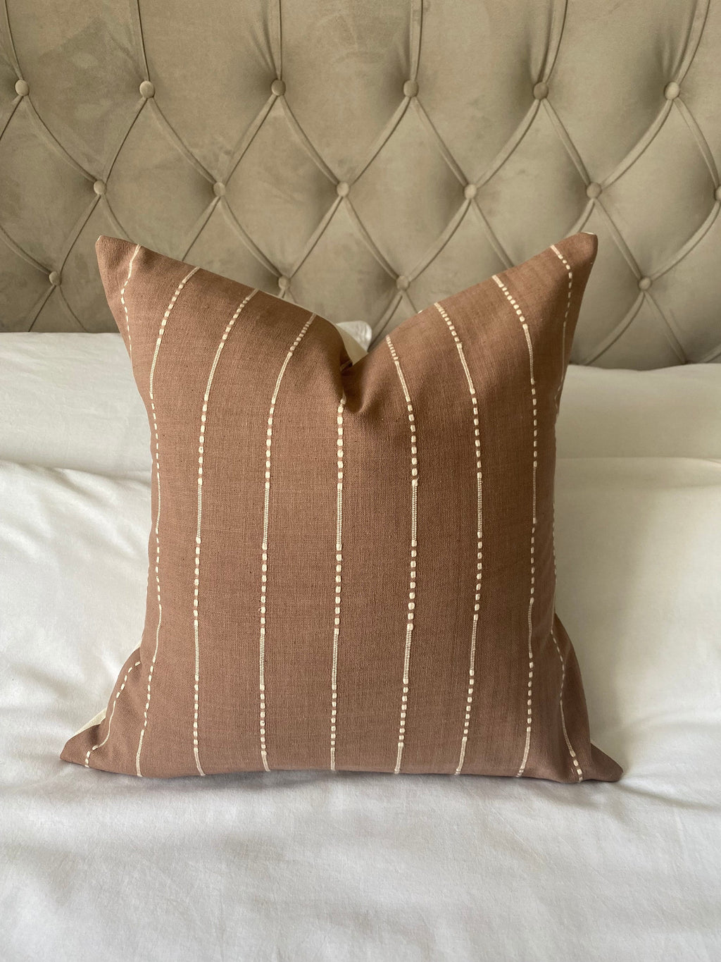 tan Brown pillow with white stripes on a bed with a tufted headboard