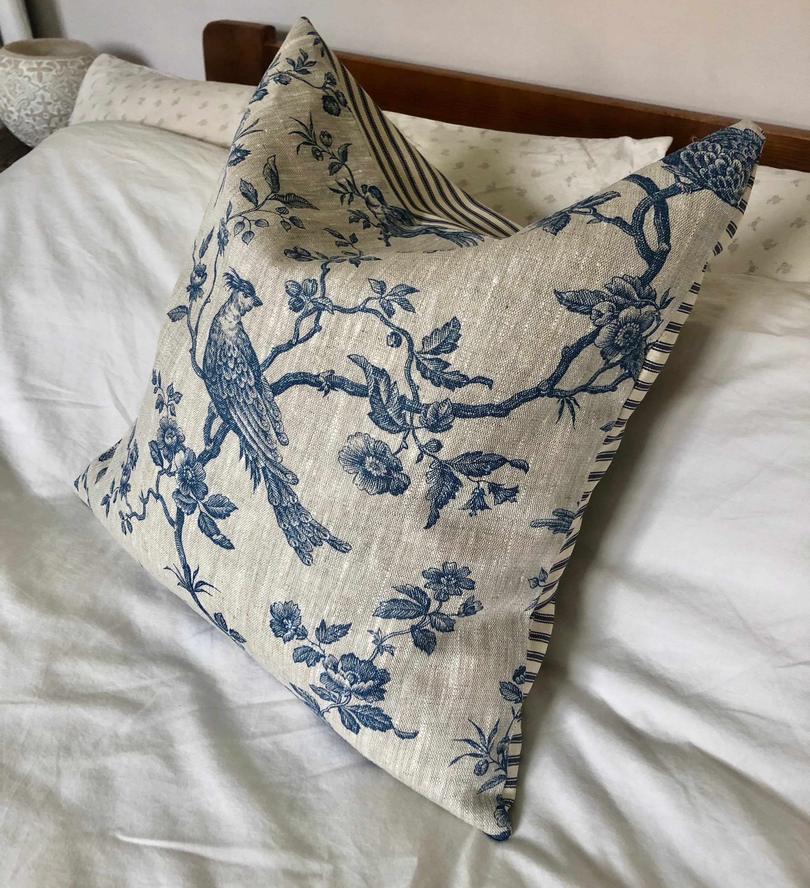 Decorative linen pillow with blue bird and floral pattern on a bed