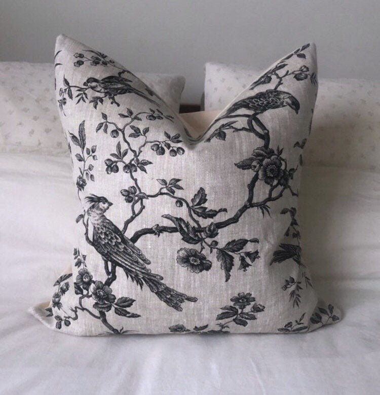 Decorative pillow with black floral and bird pattern on a light beige background