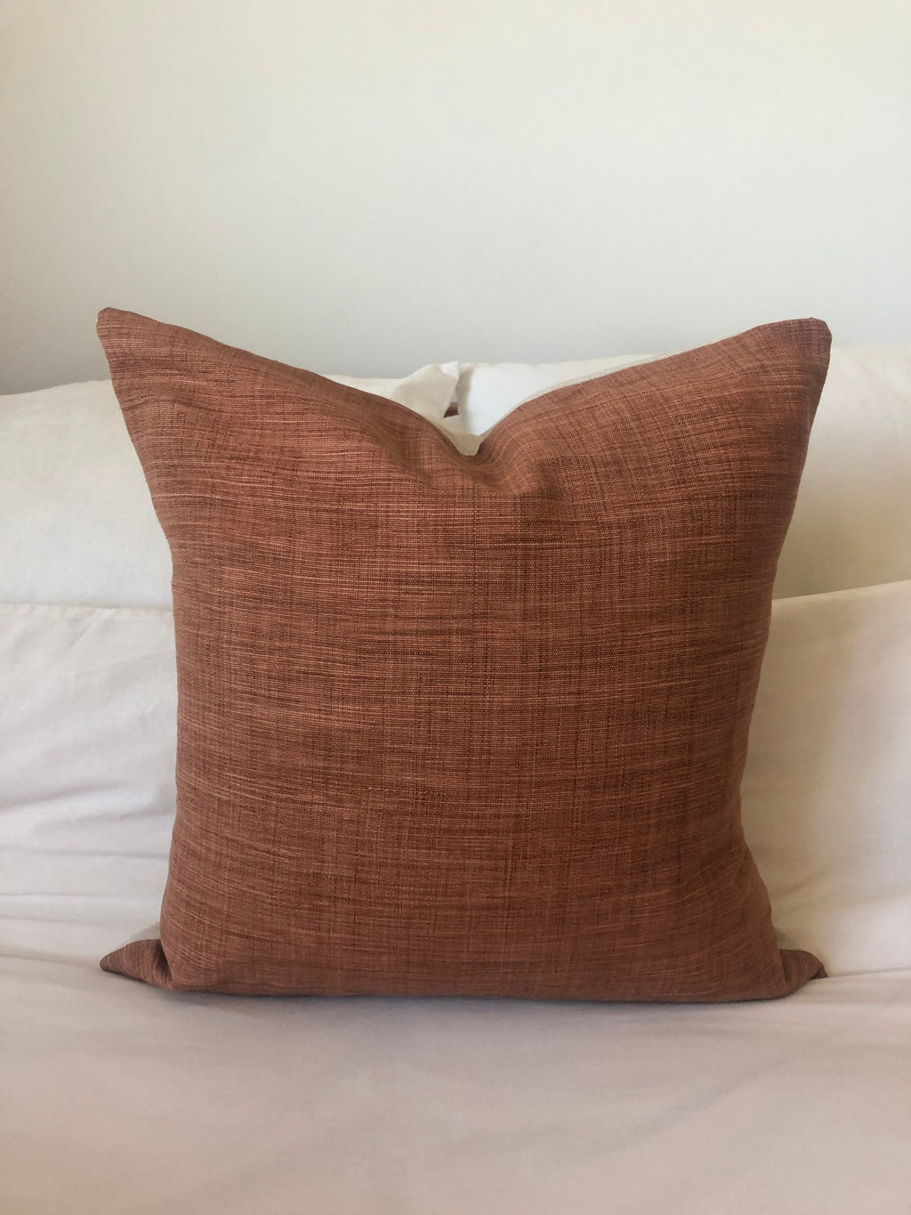 rust orange textured pillow on a white bed