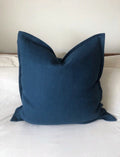 Petrol blue linen cushion cover with envelope closure on a neutral bed
