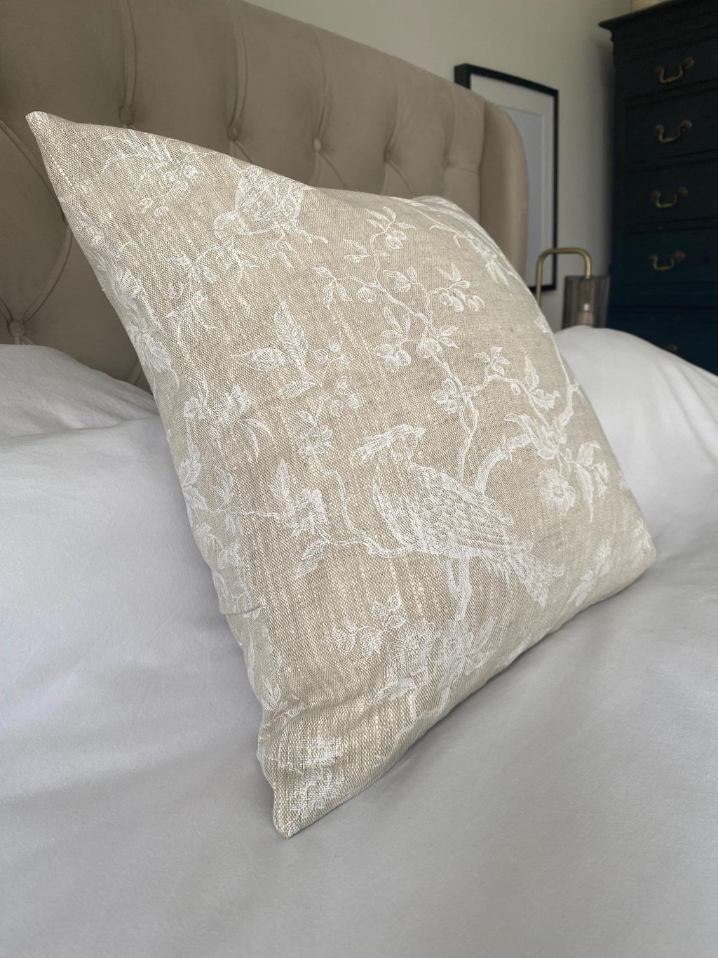 Decorative beige linen pillow with floral pattern on a bed in a bedroom setting
